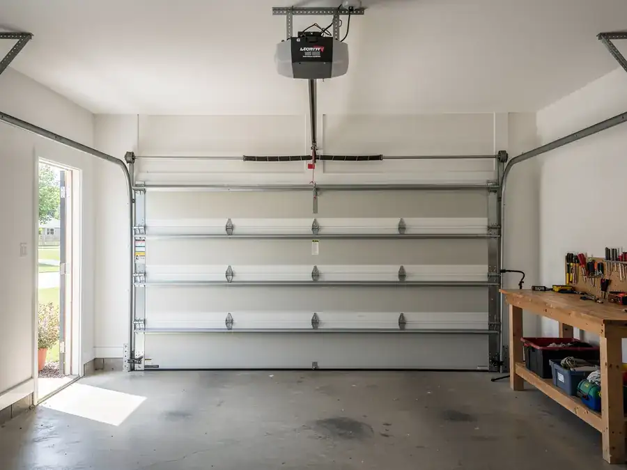 A closed garage door with an opener, tracks, and a workbench.