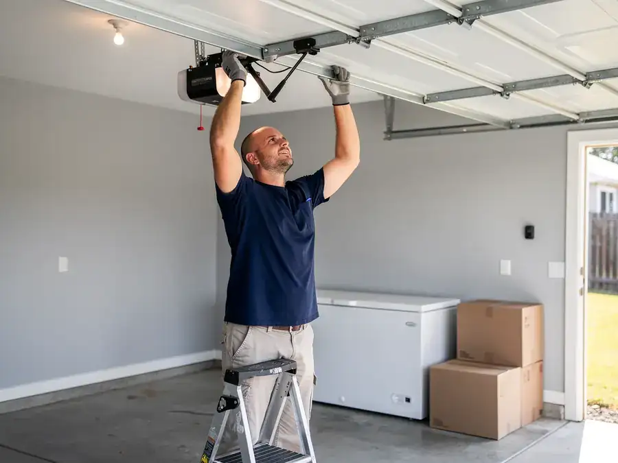 A technician on a ladder is installing a garage door opener.