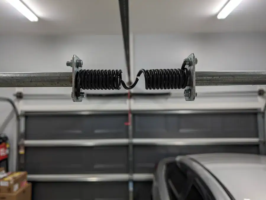 A broken torsion spring is visible on a metal rod above a garage door.